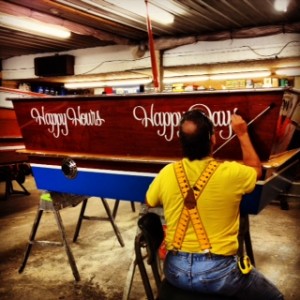 A picture of a man painting lettering on the back end of a boat